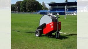 Sistema di irrigazione automatico a rullo Orma Leader posizionato sul prato verde di uno stadio con tubo srotolato.