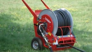 Attrezzatura compatta e portatile per l'irrigazione del giardino su prato verde, che include due avvolgitubo carrellati colorati e un carrello sprinkler separato, con una casa sullo sfondo.