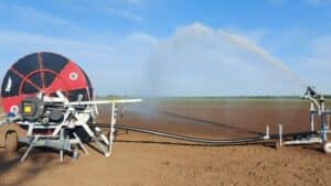 Irrigatore semovente a tamburo Orma Srl modello Event collegato al suo carrello con cannone, mentre lancia un potente getto d'acqua a pioggia su un grande terreno arato