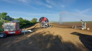 Impianto completo per irrigazione agricola Orma Srl in azione composto da un gruppo motopompa carrellato, un irrigatore semovente a tamburo e un carrello con cannone spruzzatore su terreno arato