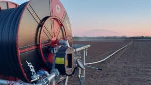 Grande rotolone irrigatore Orma Event posizionato in un terreno agricolo arato durante le ore serali, con tubo srotolato verso il cannone irrigatore sullo sfondo